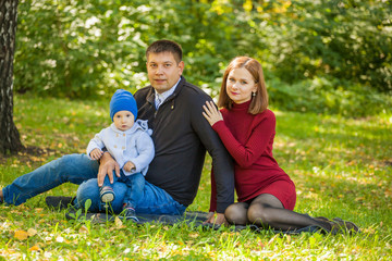 mom, dad and baby are sitting on the grass in the park. Family weekend in the fall