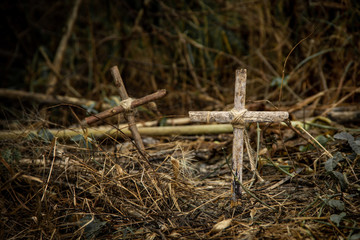 The cross is made of old wood and has a rope tied at the core in dry forest cemetery on dark background.
