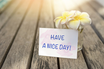 Have a nice day greeting card with beautiful Plumeria flower in glass vase on wooden floor with vintage warm light