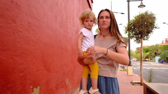 Young mother carrying her daughter and taking a walk on the street in Spain during summer day in slow motion.
