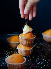 Cupcake with cream and colorful sprinkles on a dark background.