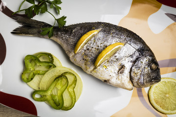 Dorada fish cooked in the oven with lemon, pimento and green onion served on a tray on a wooden table ready to eat

