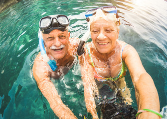 Happy retired couple taking selfie in tropical sea excursion with water camera and snorkel masks -...
