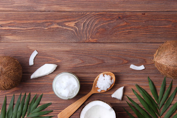 coconut oil, coconuts and green tropical leaves on wooden background. Top view.