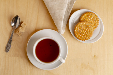 Cup of hot tea on a saucer, fresh biscuits, brown sugar and a cloth napkin.