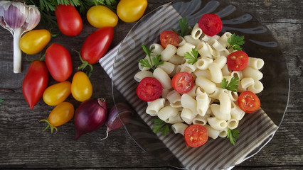 Delicious pasta with tomatoes and greens on wooden background.