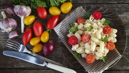 Delicious pasta with tomatoes and greens on wooden background.