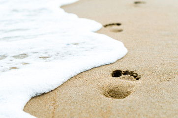 footprints in the sand on the beach near the surf