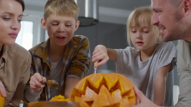 Little boy and girl removing the filling from carved pumpkin and talking with mom and dad while preparing for Halloween