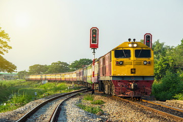 Procession train led by Yellow Diesel electric Locomotives at curve and sail through rail chopper with traffic light before entering Ratchaburi station of Thailand.