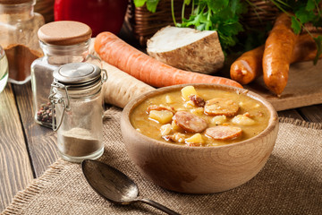 Wooden bowl of split pea soup with sausage and potatoes