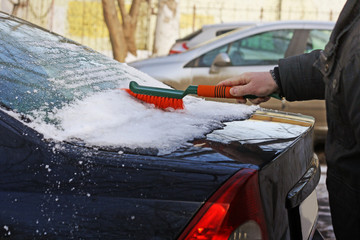 Man brush cleans the car from snow.