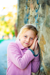 A young girl in a pink coat is leaning against a wall, rubbing in close up.