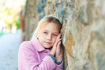 A girl in a pink coat stands near the wall, rubbing close-ups.