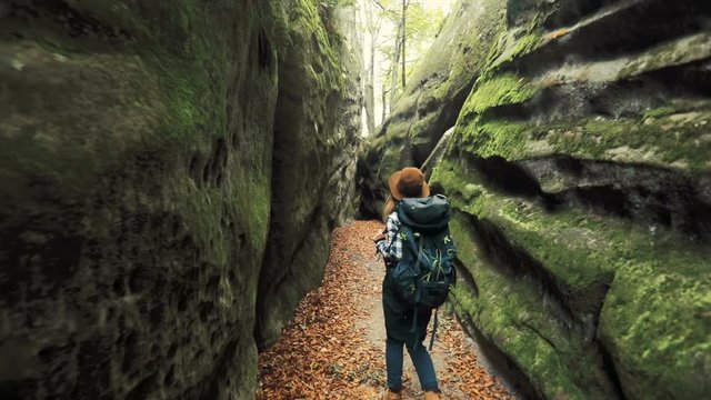 Curious, smiling girl wandering around the cave, cheking out moss-covered, massive stones on warm, sunny day
