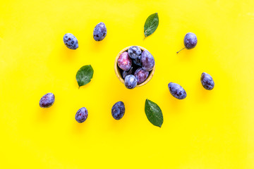 Blue plum for dessert. Purple plum and leaves pattern on yellow background top view copy space