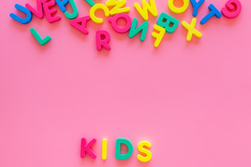 Early childhood development concept. Word kids written by plastic letters of toy alphabet on pink background top view copy space