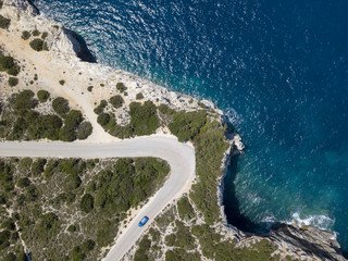 Aerial car driving on coastal cliff edge road corner