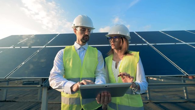 Two workers stand on solar panels background, close up.
