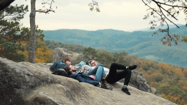 Group of friends watching wonderful mountain sky, enjoying freedom of open spaces as lying on big solid rock