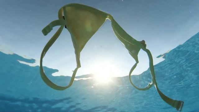 Sun shines over floating bikini, slow motion