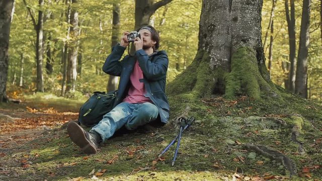 Male photographer taking photos in the forest, sitting by moss-covered tree on warm, fall day