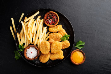 Chicken nuggets and french fries with various sauces on a black background. Top view