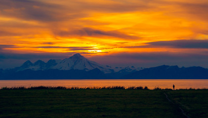 A figure watches the sunset over Mount Illiamna and Cook Inlet in Ninilchik, Alaska