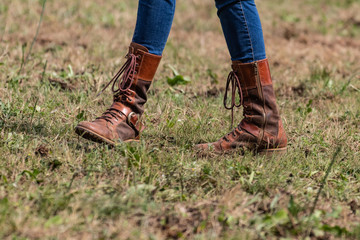 Beautiful slim legs in tight blue jeans. Country cow girl with brown leather boots walking on dry grass, end of season moments. Farm life, stylish woman..