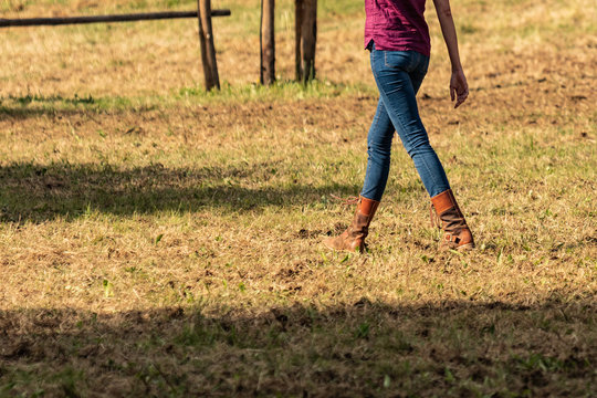 Beautiful Slim Legs In Tight Blue Jeans. Country Cow Girl With Brown Leather Boots Walking On Dry Grass, End Of Season Moments. Farm Life, Stylish Woman..