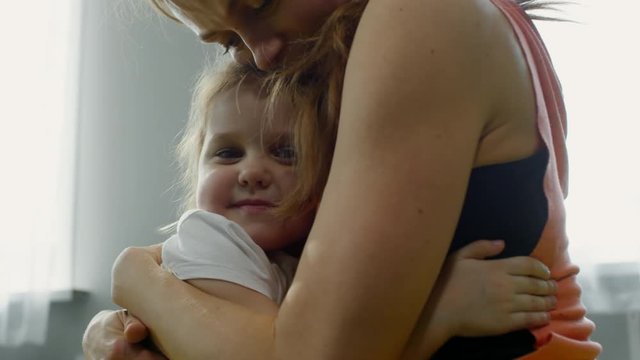 Medium shot of young mother and cute preschool-age girl hugging tightly and smiling