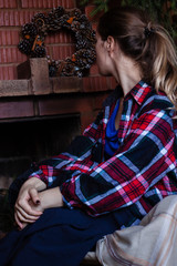 Fototapeta premium young woman in checkered shirt near the red brick fireplace. Christmas winter time