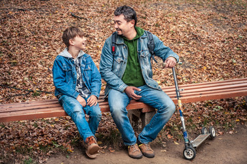 Happy dad and son talking in the autumn park on a bench. Family holiday