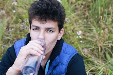 The teen is drinking water sitting on the ground and resting after doing sports on the street. Top view