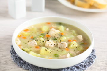 Chicken and potato chowder soup with green bell pepper and carrot in bowl, photographed with natural light (Selective Focus, Focus on the chicken pieces one third into the soup)