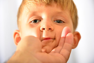 Closeup portrait of boy, little man's hand holds baby by the face.