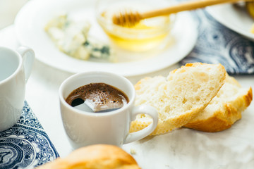  couple of cups with coffee, cheese, honey, baguette and fruit on a light marble table