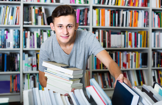 portrait of  boy standing among bookshelves and searching for book in library