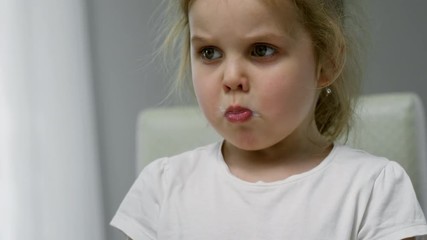 Medium shot of adorable little girl chewing mouthful of cereal and talking
