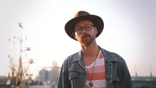 Portrait of stylish hipster bearded man in hat and glasses smoking cigarette outdoors
