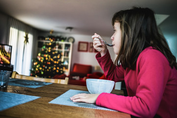 Young girl eating breakfast cereals and watching television in the living room at christmas time....