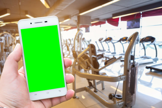 Close-up Men use Hand holding smartphone blurred images touch of Abstract blur of defocused sport gym interior and fitness health club with sports exercise equipment Gym blur background.