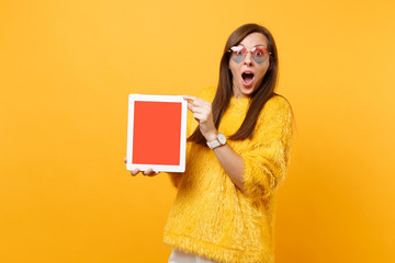 Excited shocked young woman in heart glasses holding tablet pc computer with blank black empty screen isolated on bright yellow background. People sincere emotions lifestyle concept. Advertising area.