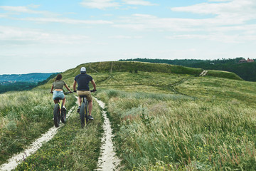 Young couple are cycling at the green hills. Rear view