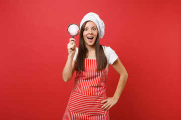 Housewife female chef cook or baker in striped apron white t-shirt toque chefs hat isolated on red wall background. Housekeeper woman hold and look through magnifying glass. Mock up copy space concept
