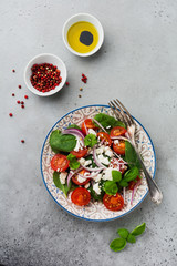 Tomatoes, spinach leaves, red onions and feta cheese salad on light ceramic plate on gray backround. Selective focus. Top view.