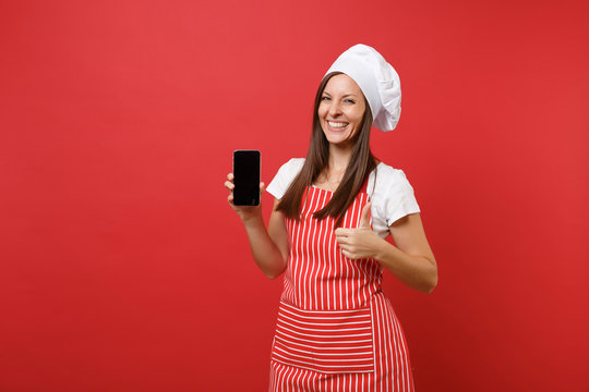 Housewife female chef cook or baker in striped apron white t-shirt toque chefs hat isolated on red wall background. Woman hold cellphone blank screen for promotional content Mock up copy space concept