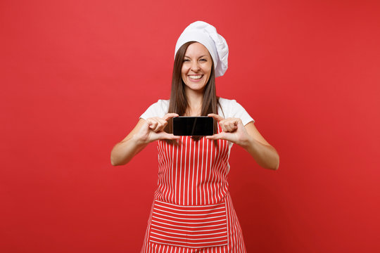 Housewife female chef cook or baker in striped apron white t-shirt toque chefs hat isolated on red wall background. Woman hold cellphone blank screen for promotional content Mock up copy space concept