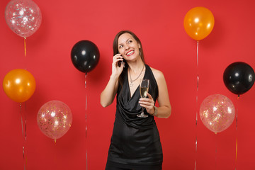 Pretty girl in black dress holding glass of champagne talk on mobile phone conducting pleasant...