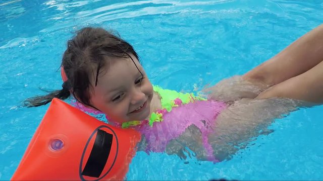 Child in the pool. Little girl plays with dad in the pool.
